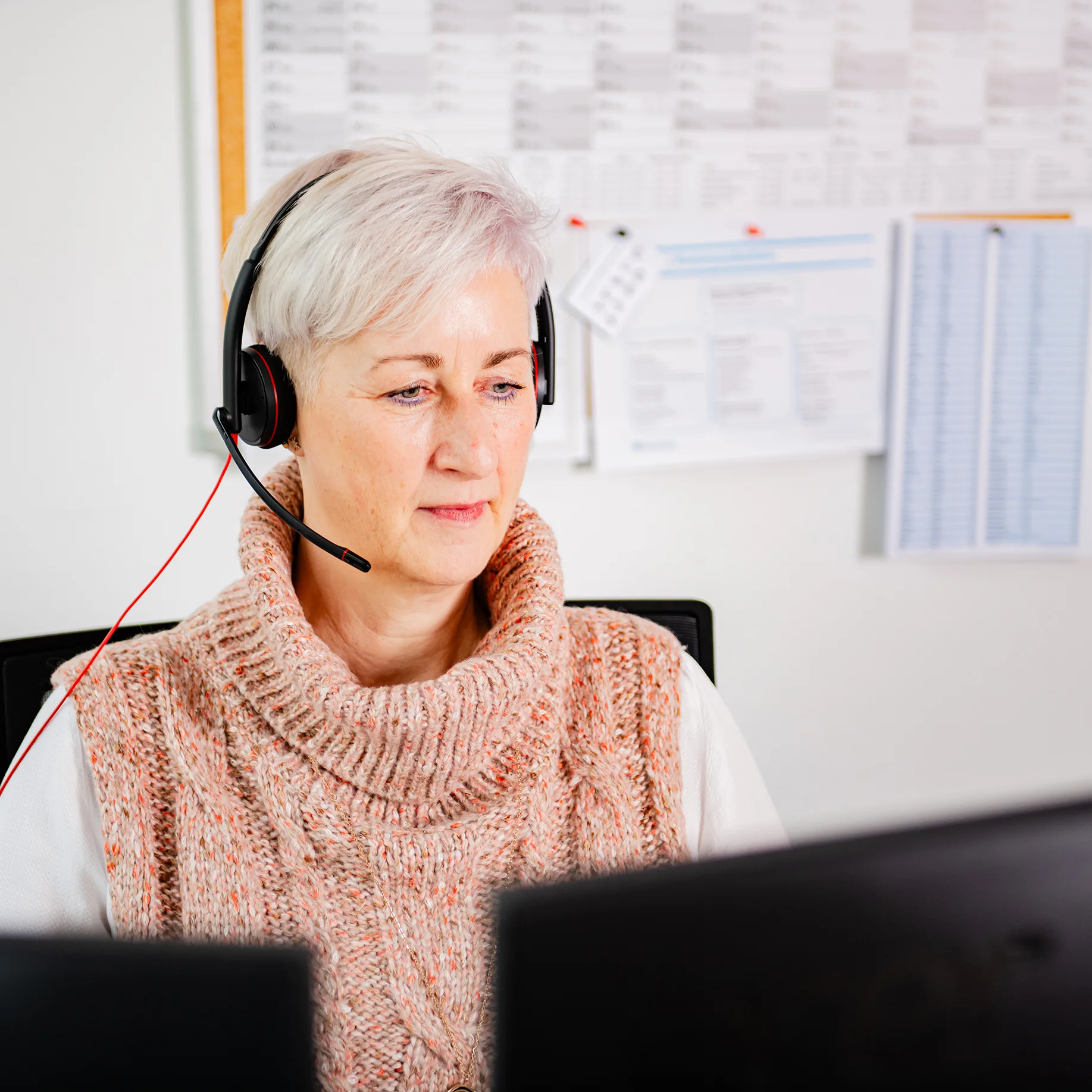 Frau mit Headset sitzt vor zwei Monitoren.