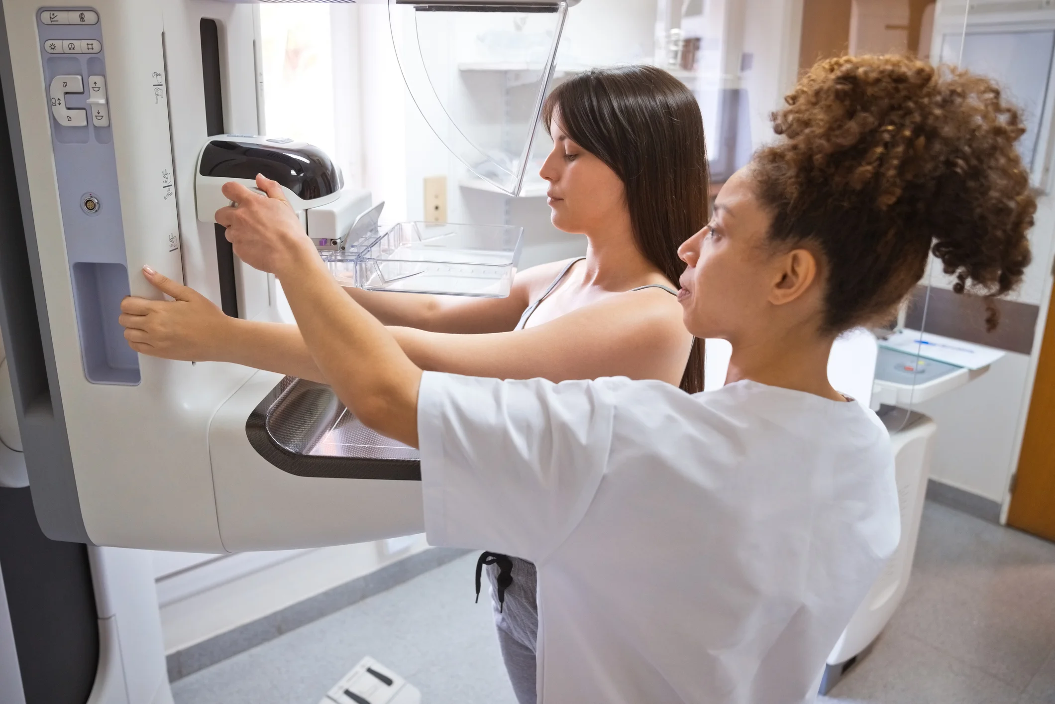 Eine medizinische Fachkraft unterstützt eine Patientin bei der Positionierung ihrer Brust an einem Mammographiegerät.
