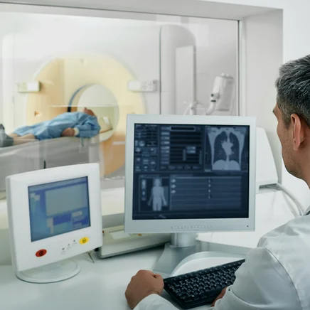 Radiologe überwacht am Computer eine CT-Untersuchung der Lunge bei einem liegenden Patienten.