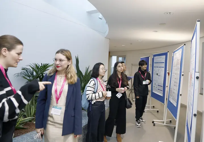 Teilnehmende der ICCP betrachten wissenschaftliche Poster. Eine Frau erklärt einer Gruppe von jungen Wissenschaftlerinnen Details zu einer Forschung.