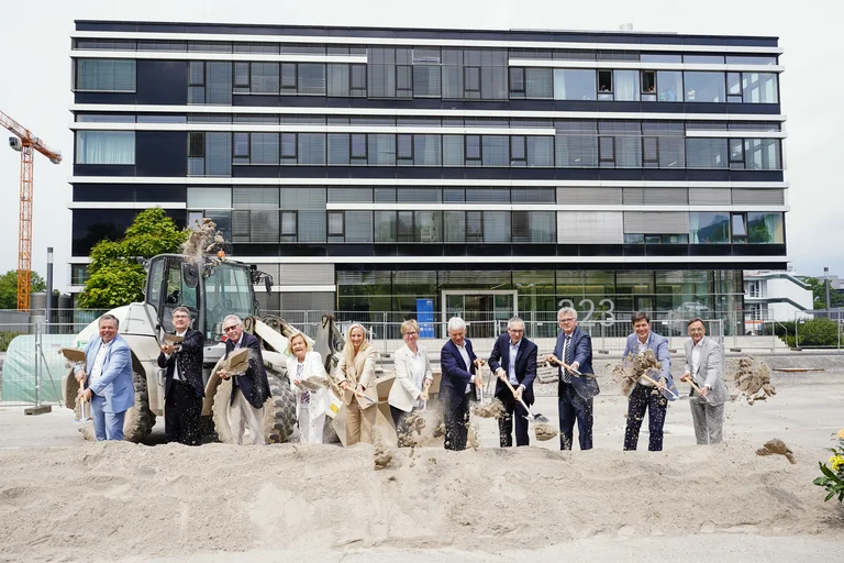 Zwölf Personen werfen vor dem Gebäude des Radiologischen Entwicklungszentrums mit Schaufeln Sand in die Luft.