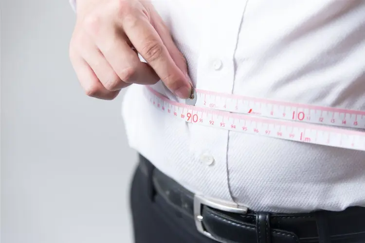 Mann hält ein Maßband um den Bauch.