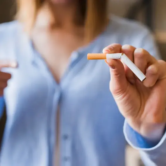 Eine Person hält eine Zigarette in der Hand und zeigt mit dem Daumen nach oben. Der Fokus liegt auf der Zigarette und der positiven Körpersprache.