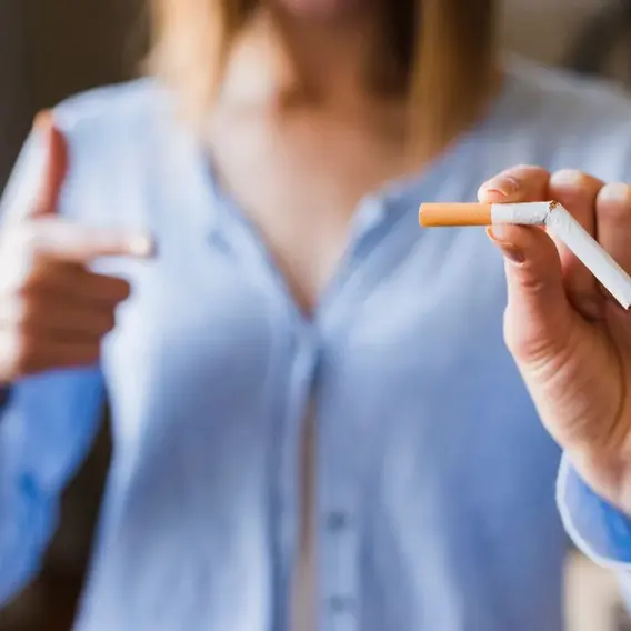 Eine Person hält eine Zigarette in der Hand und zeigt mit dem Daumen nach oben. Der Fokus liegt auf der Zigarette und der positiven Körpersprache.