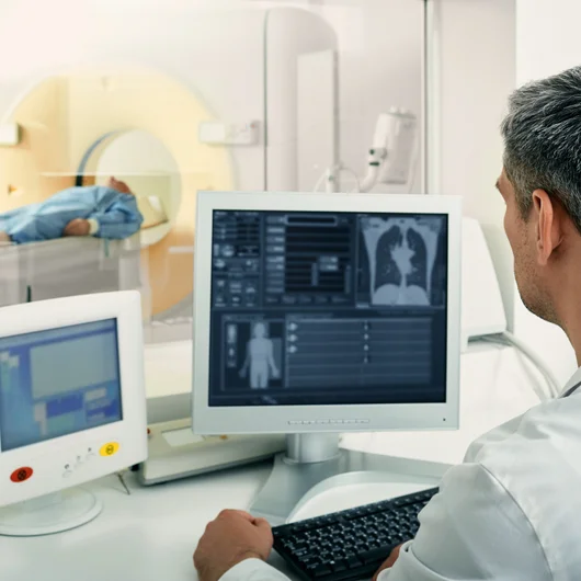 Radiologe überwacht am Computer eine CT-Untersuchung der Lunge bei einem liegenden Patienten.